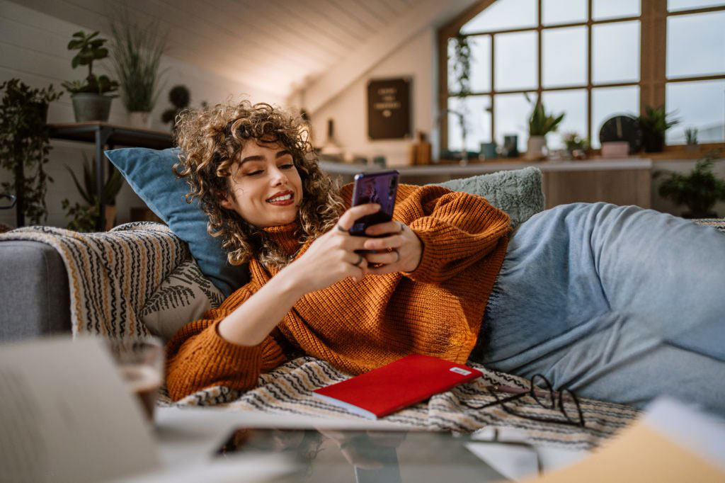 Femme souriante qui regarde son téléphone sur son canapé