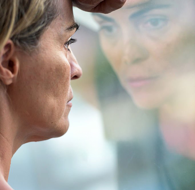 Femme épuisée en introspection devant sa fenêtre