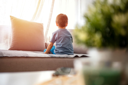 Enfant assis calmement de dos sur un canapé, dans une lumière douce, illustrant un temps de pause éducatif après une colère.