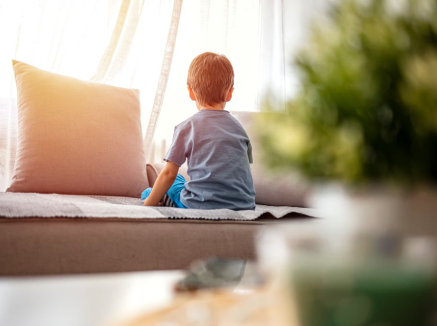 Enfant assis calmement de dos sur un canapé, dans une lumière douce, illustrant un temps de pause éducatif après une colère.